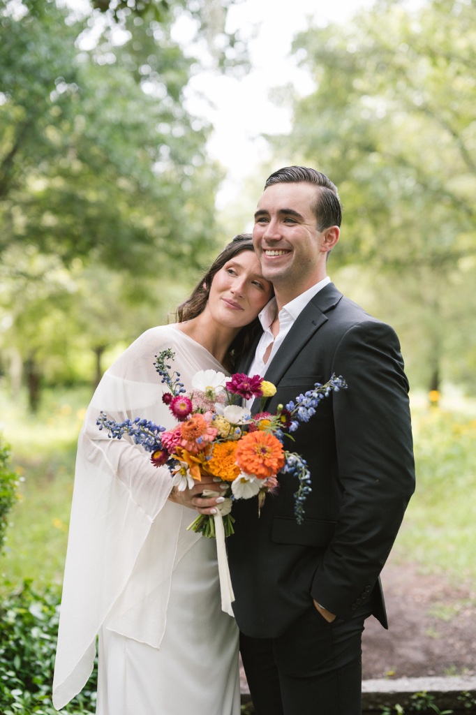 Couple embracing in garden with colorful zinnia and delphinium bouquet