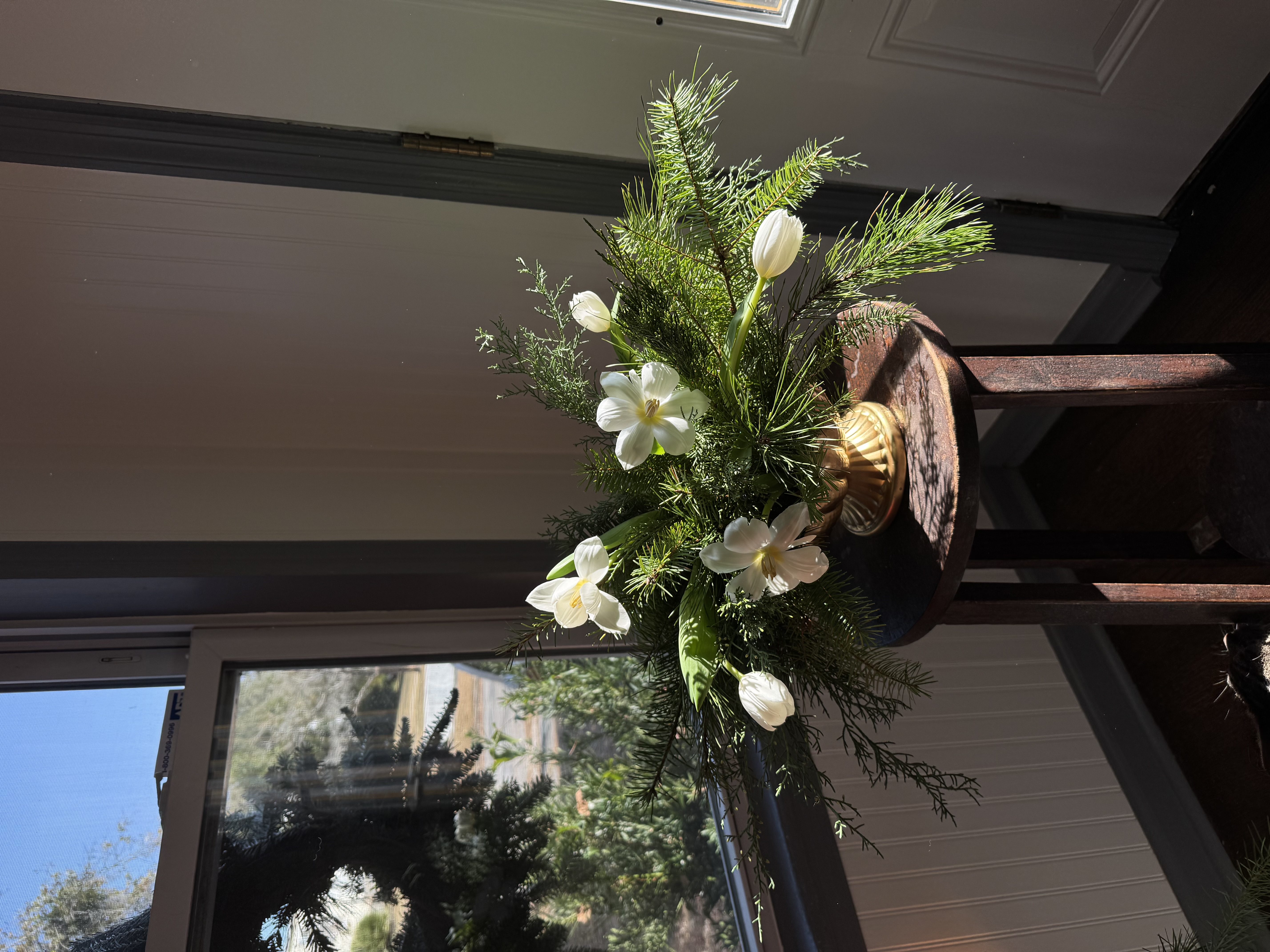 White tulip and narcissus arrangement with pine sprigs mounted on a wooden post in natural light