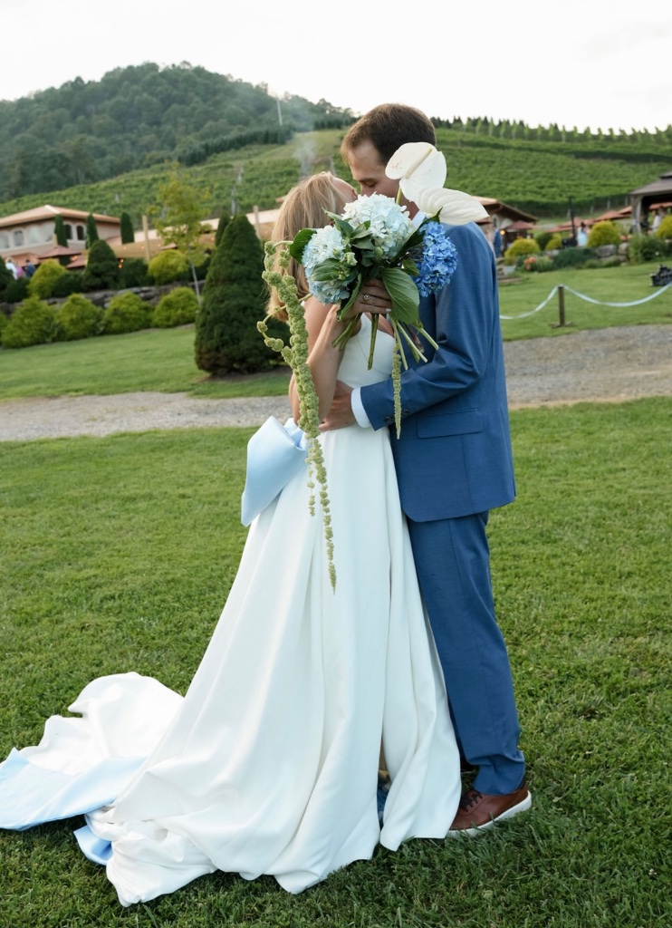 Bride and groom kissing at vineyard wedding with blue hydrangea bouquet