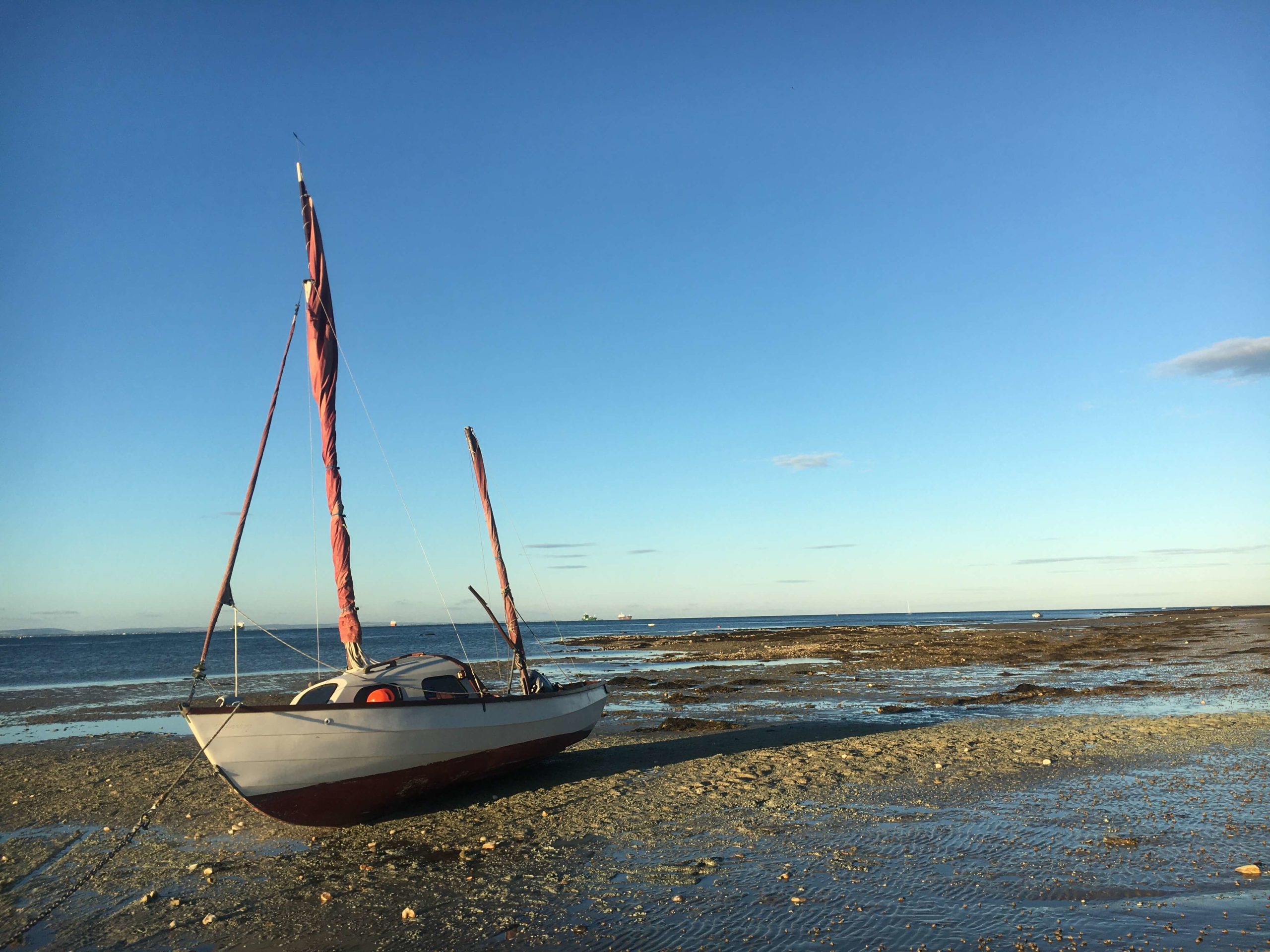 A small sailboat grounded on the beach at Bembridge at low tide