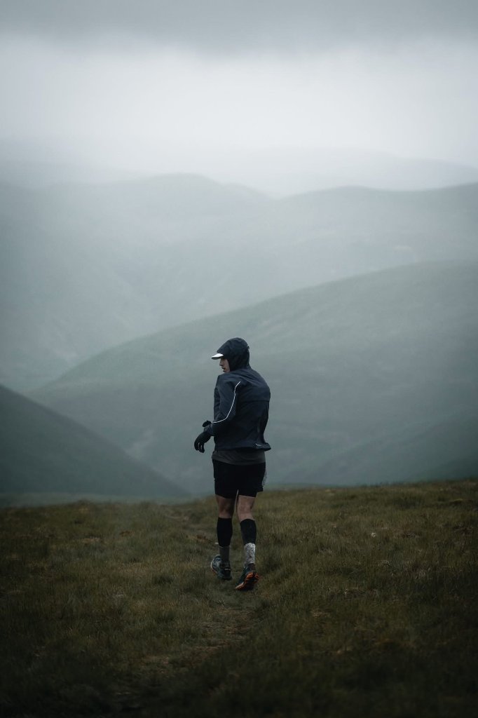 DVOTION founder Chris Gkoufas on the Scottish Highlands during Ultra Scotland 104-mile race, standing amid misty hills