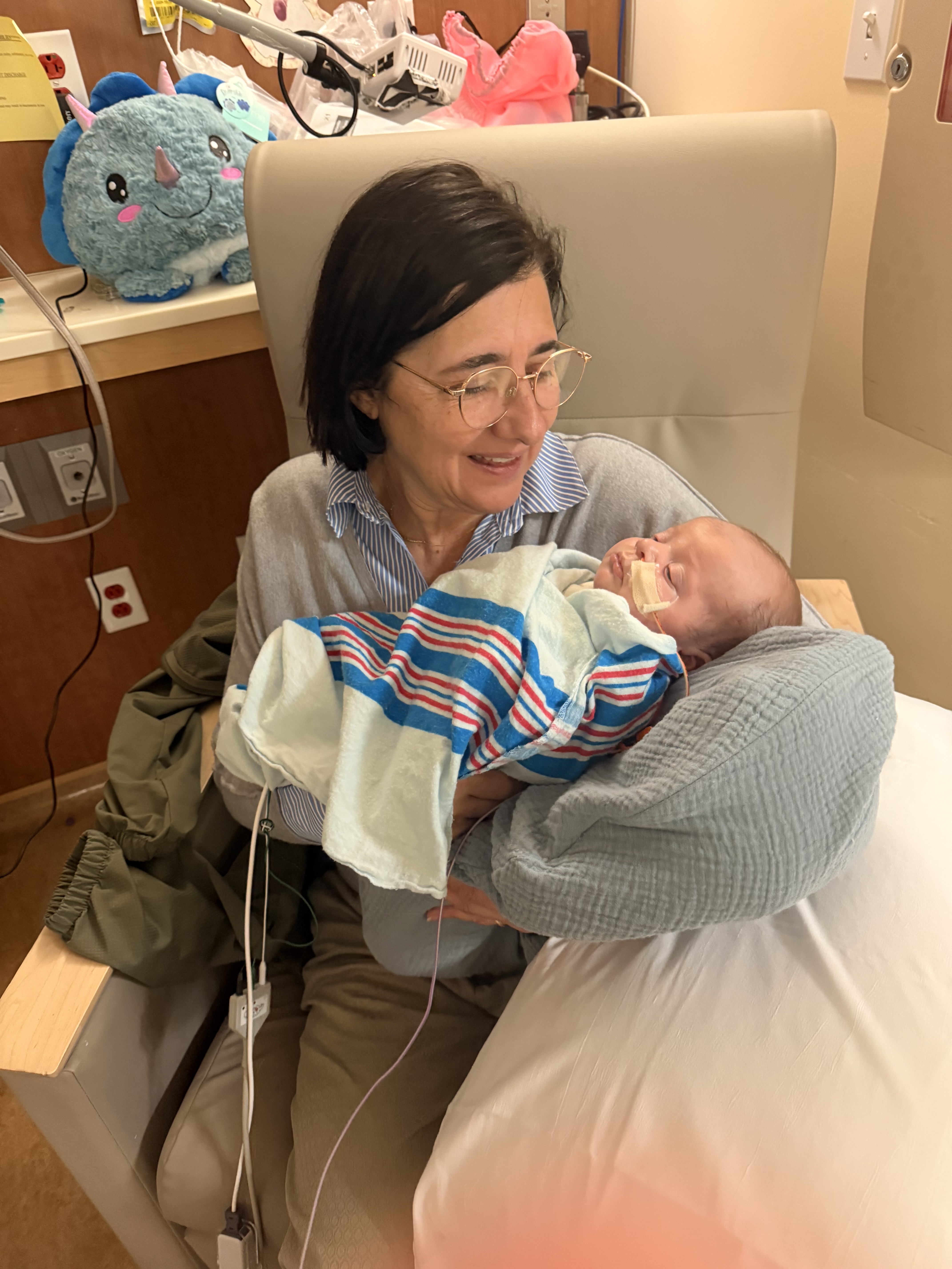 Marisa holding a newborn baby wrapped in a striped hospital blanket, cradled on a nursing pillow