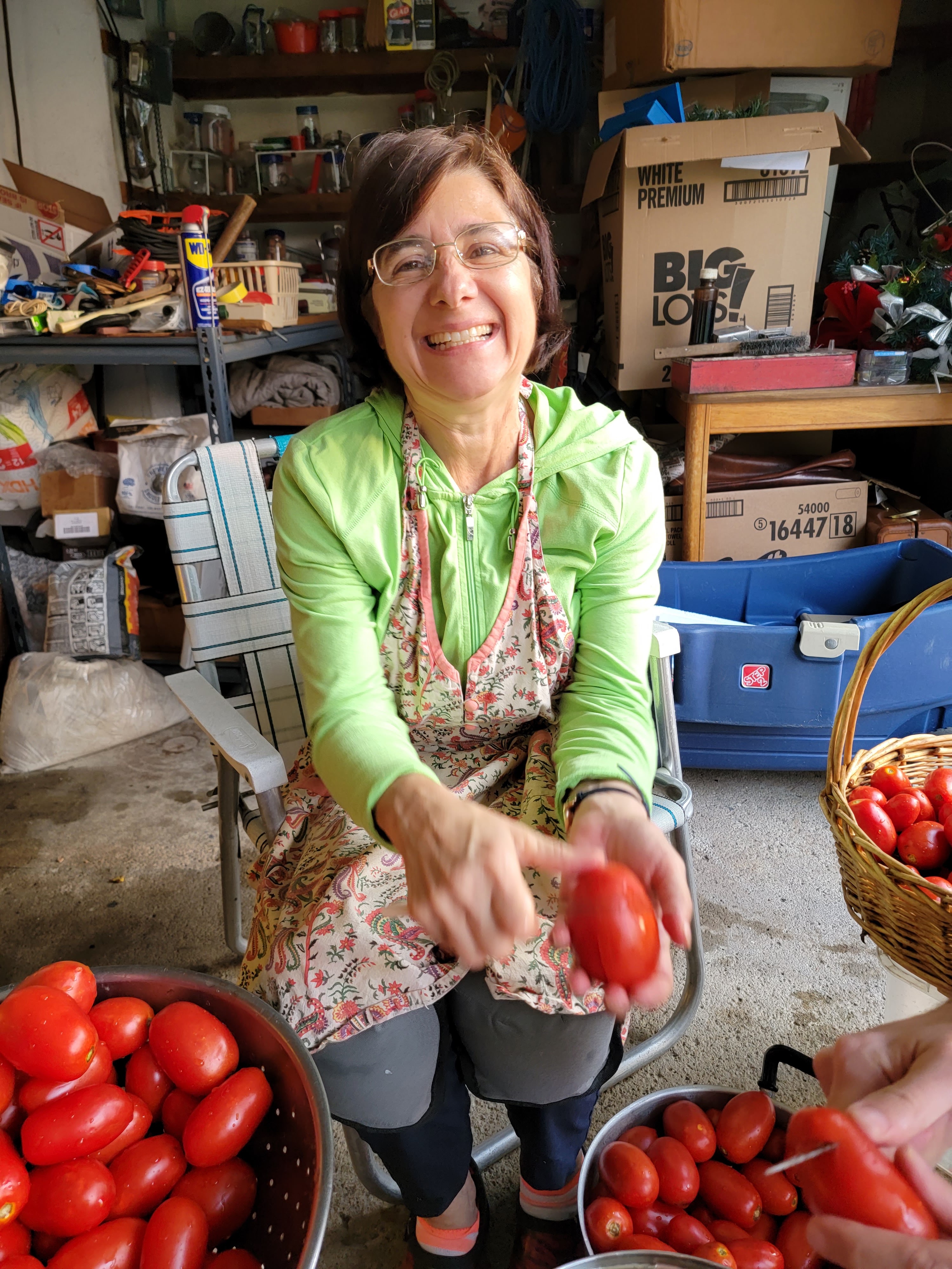 Marisa smiling in her garage during tomato-preserving season, baskets of tomatoes around her