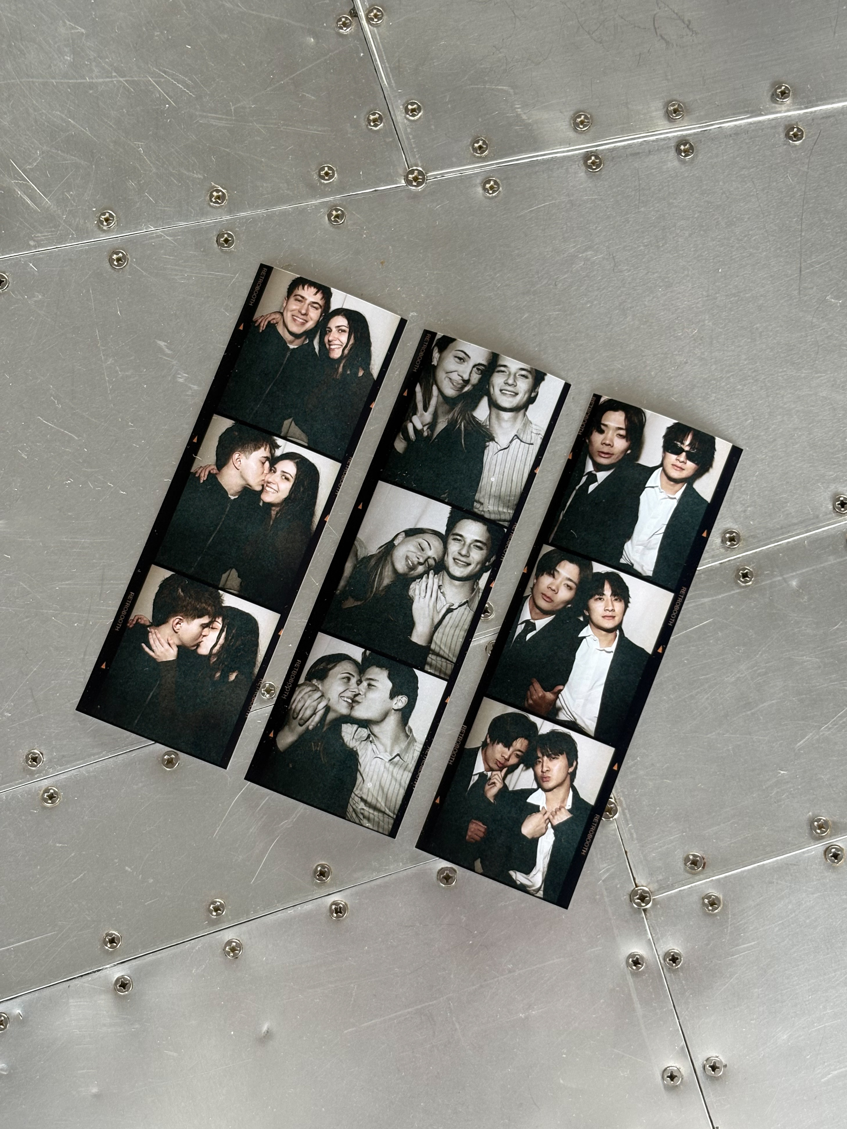 Three black and white photo strips from The Retro Booth laid out on a metal surface, each showing a different group of friends