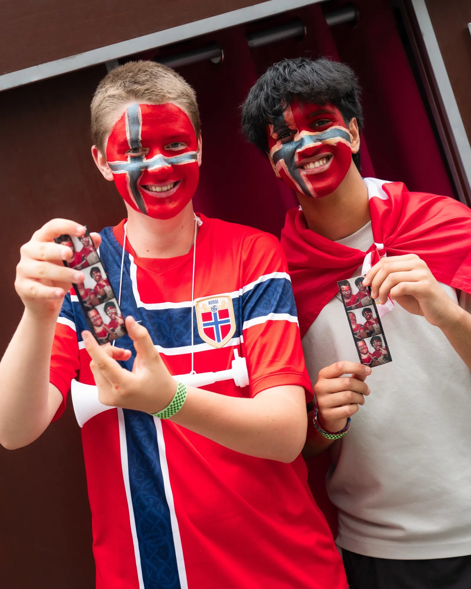 Two friends with face paint and jerseys holding Retro Booth photo strips at the FIFA World Cup fan event in Vancouver
