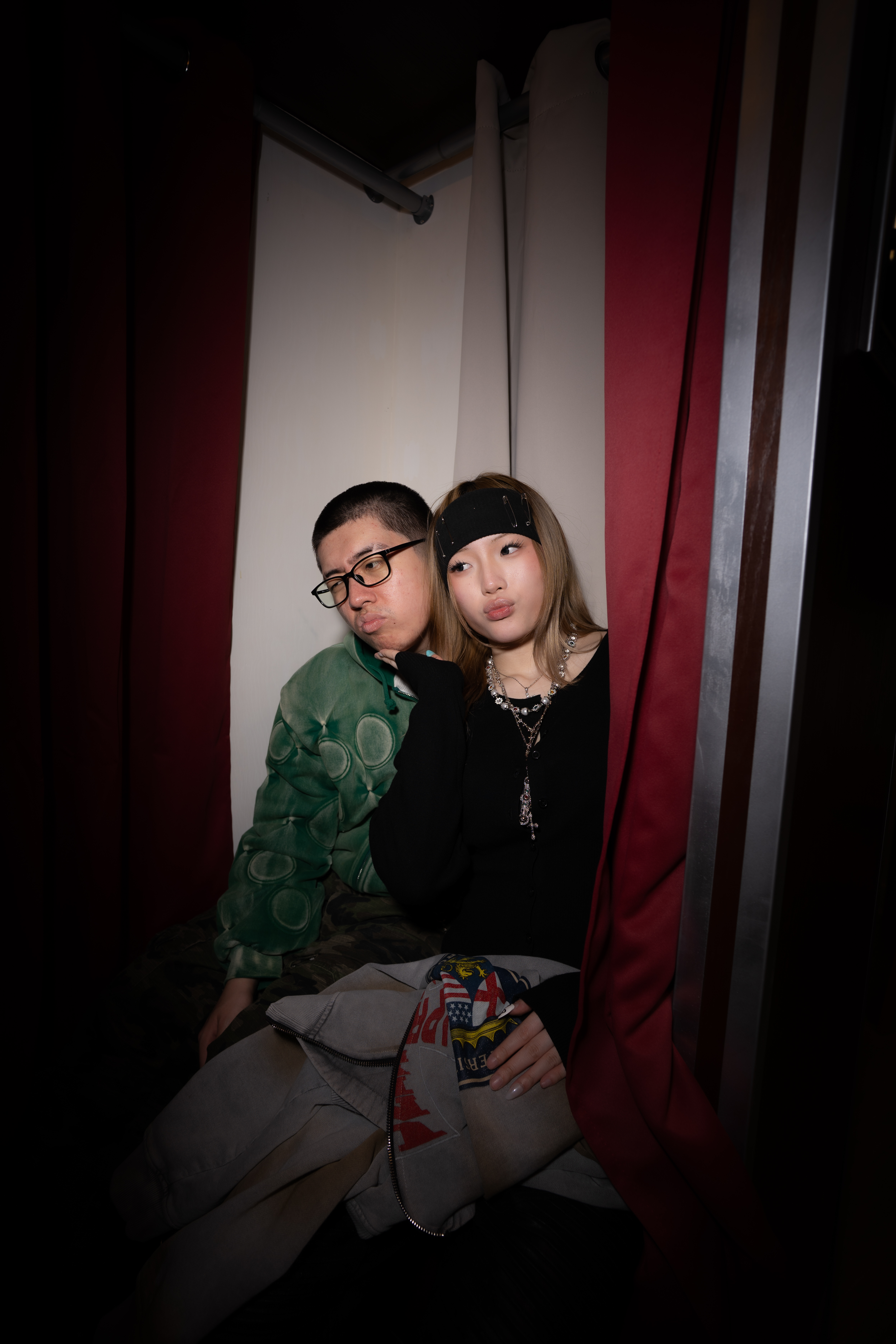 Two guests making playful faces inside The Retro Booth's enclosed vintage photo booth, red curtain visible behind them