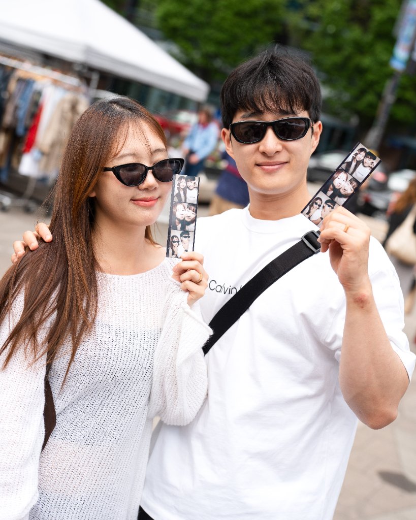 Two guests smiling outdoors, each holding a printed vintage-style photo strip from The Retro Booth