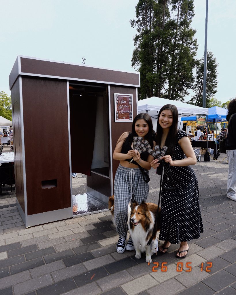 The Retro Booth's enclosed vintage photo booth set up at an outdoor Vancouver-area market event, with two guests holding photo strips and two dogs nearby