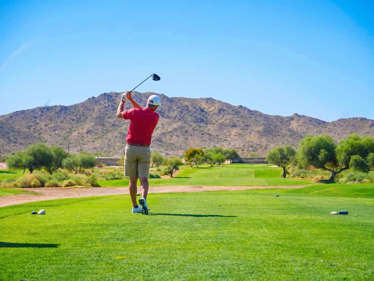 A Junior National golfer mid iron shot on a fairway with grass debris in the air and desert mountains beyond.