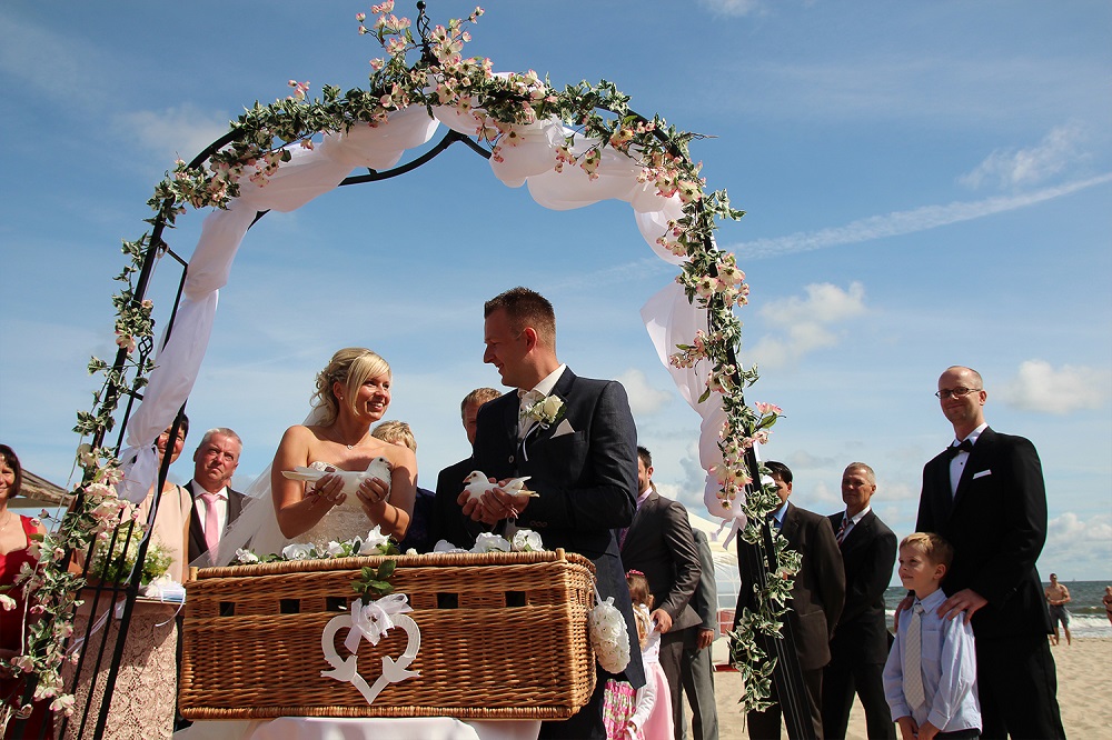Hochzeit am Strand Cliff Hotel Rügen – Brautpaar unter romantischem Blumenbogen mit Tauben