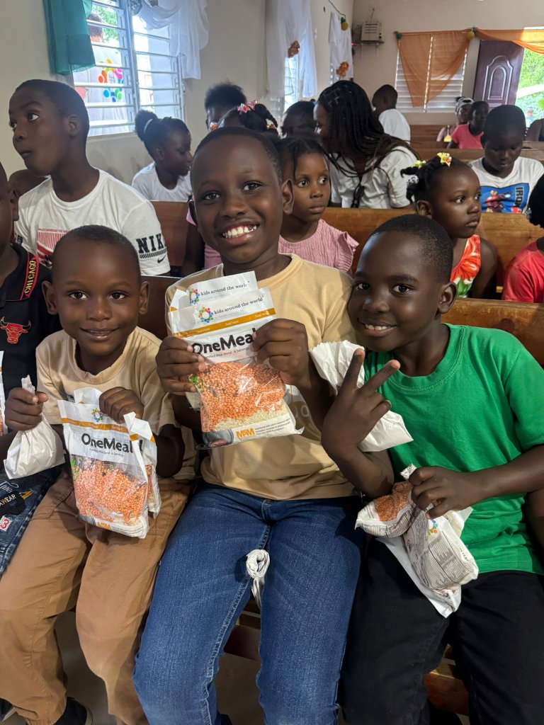Three children smiling and holding OneMeal bags from Kids Around the World