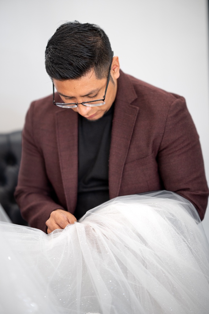 Renoj working on a white tulle wedding dress hem