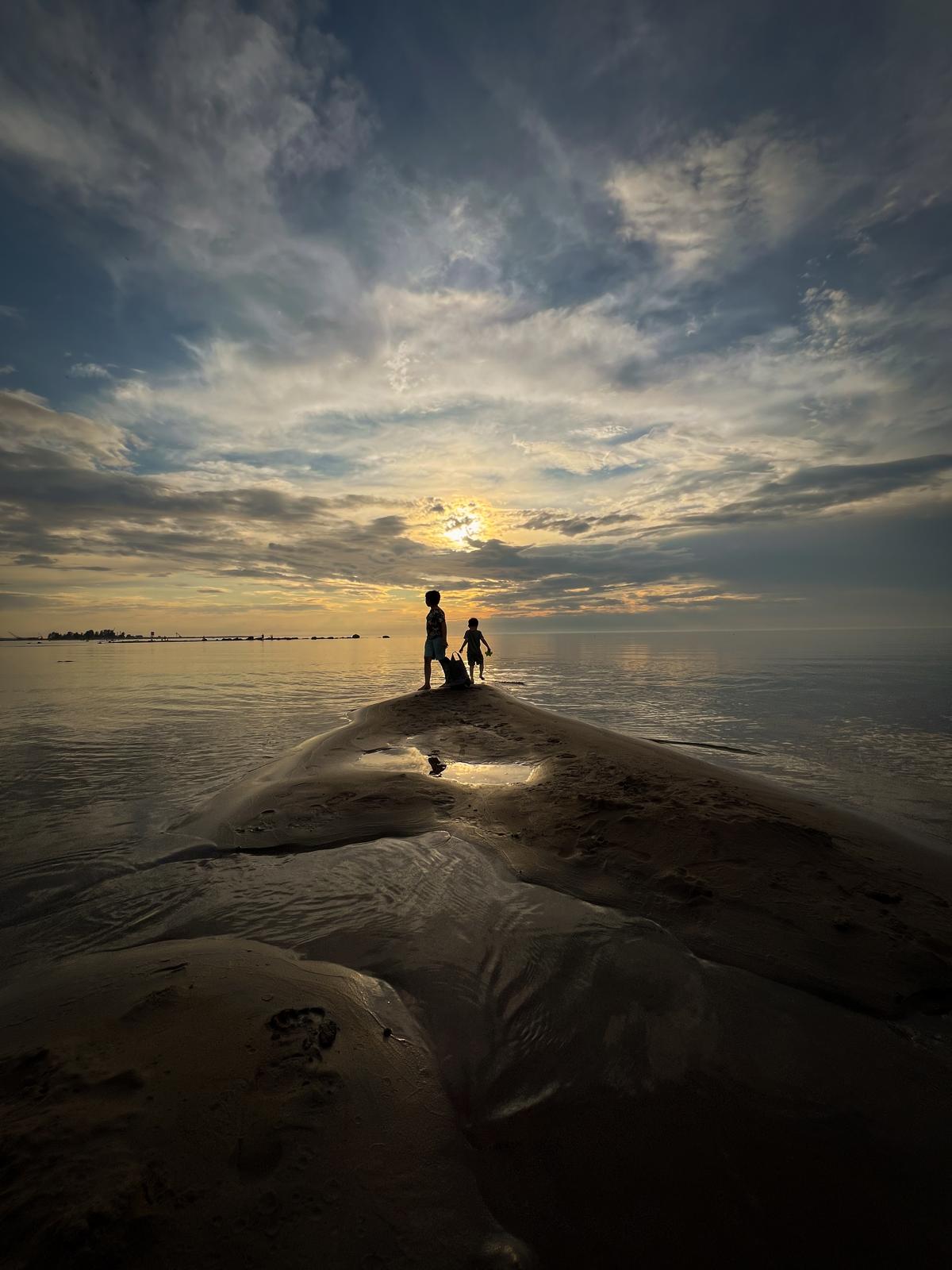 Kaksi lasta hiekkasärkällä meren rannalla auringonlaskussa