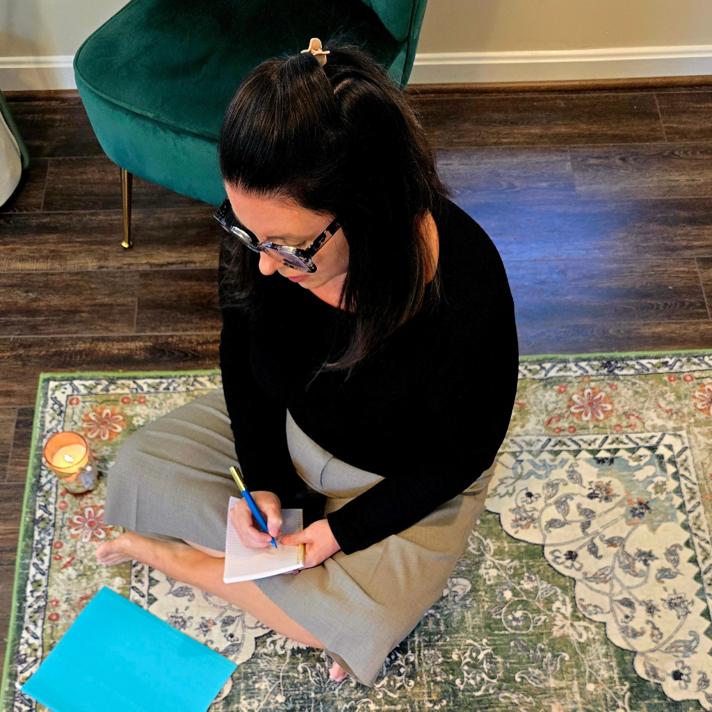 Woman sitting on a rug, writing in a notebook by candlelight