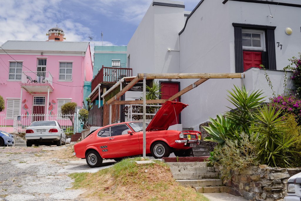A red vintage car parked outside a brightly painted house in the Bo-Kaap, Cape Town