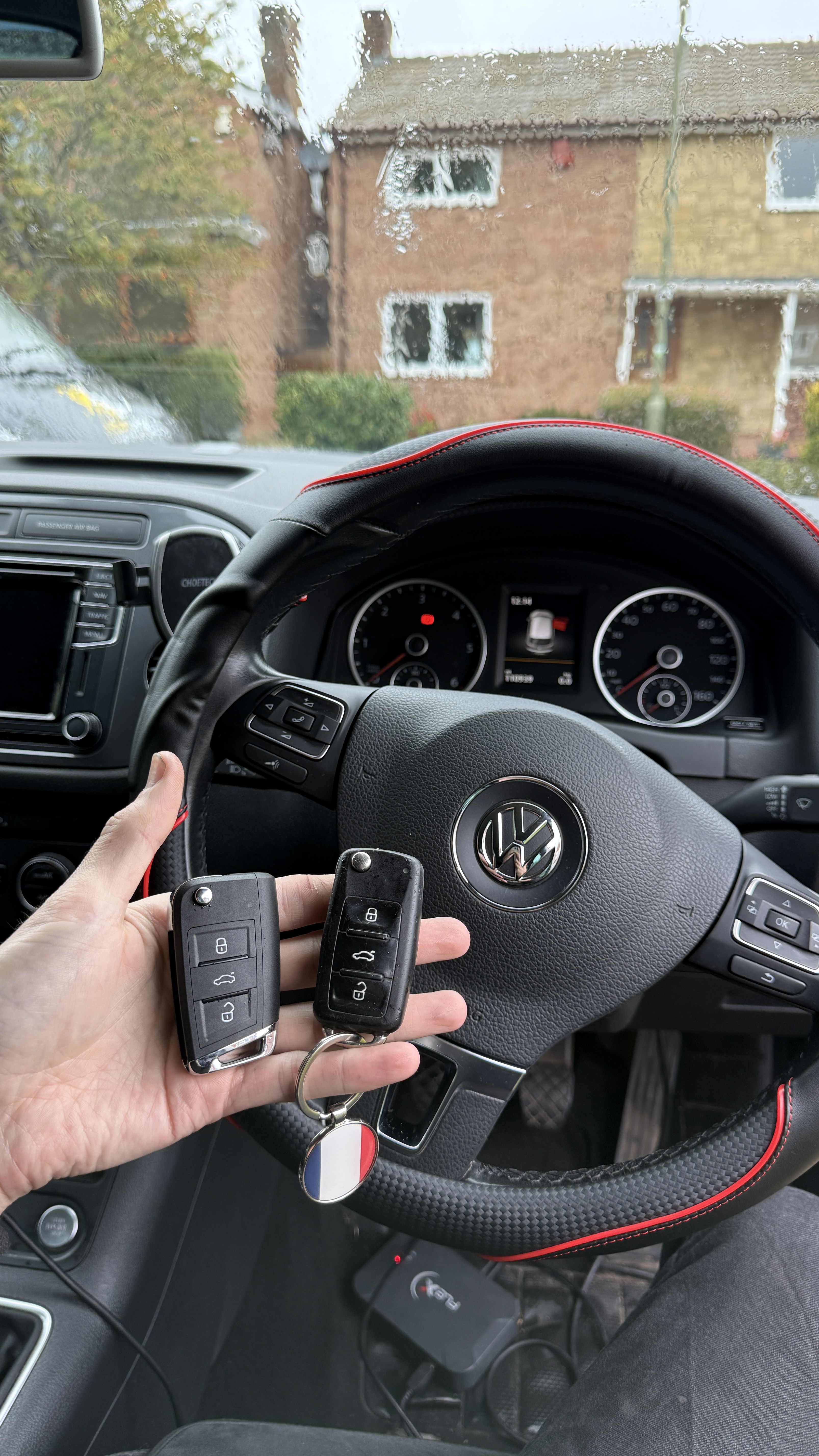 New and original Volkswagen Tiguan keyless key fobs held inside the vehicle with steering wheel visible after spare key programming by KeyLogik in Kennington, Oxford