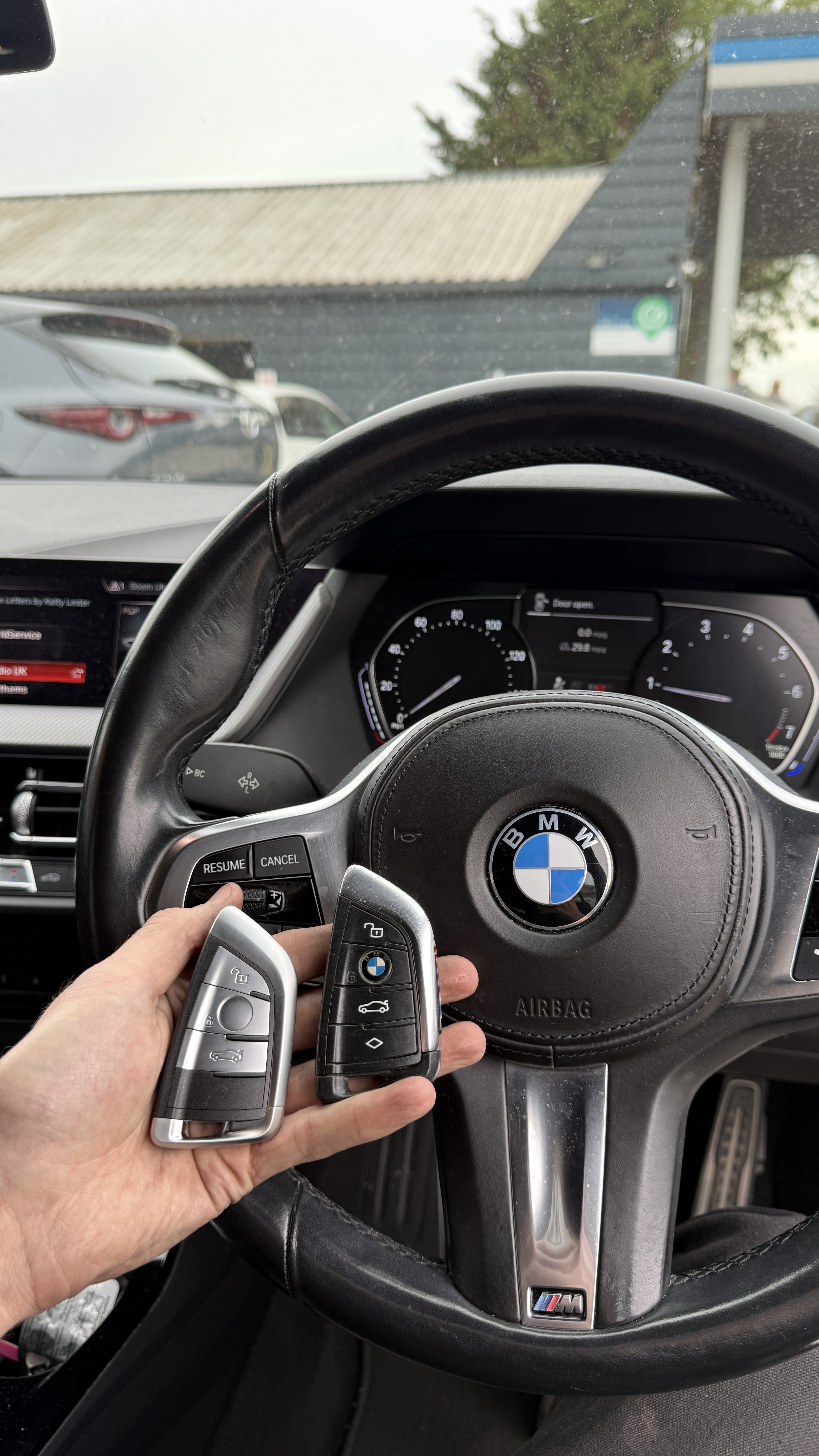 Two BMW keys held in front of the steering wheel after programming by KeyLogik