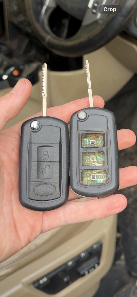 Damaged car key with button pad fallen off exposing the circuit board, next to a new replacement remote key inside the vehicle