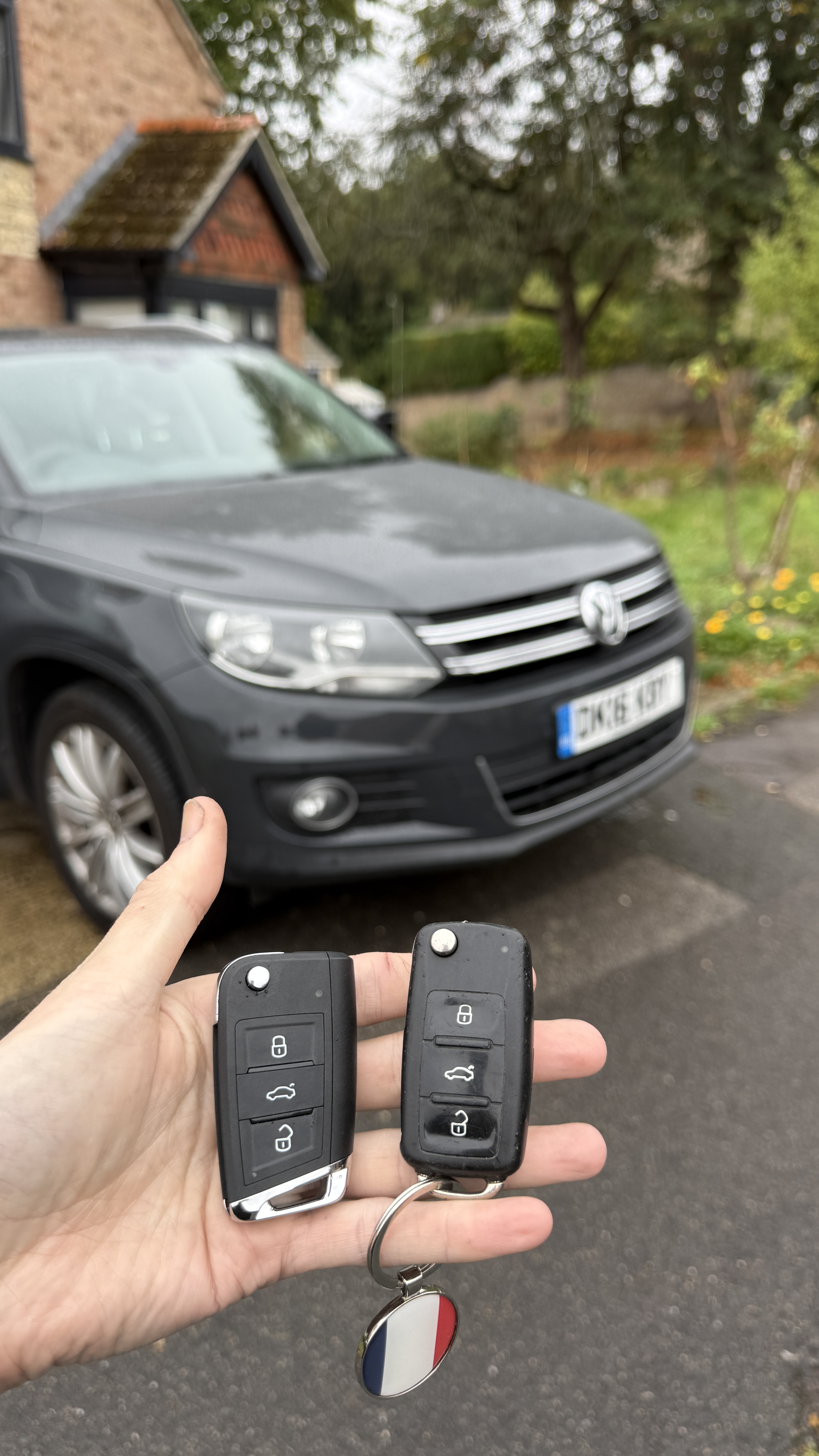 New and original Volkswagen Tiguan keyless key fobs held in front of a 2016 VW Tiguan during a spare key job in Kennington, Oxford by KeyLogik