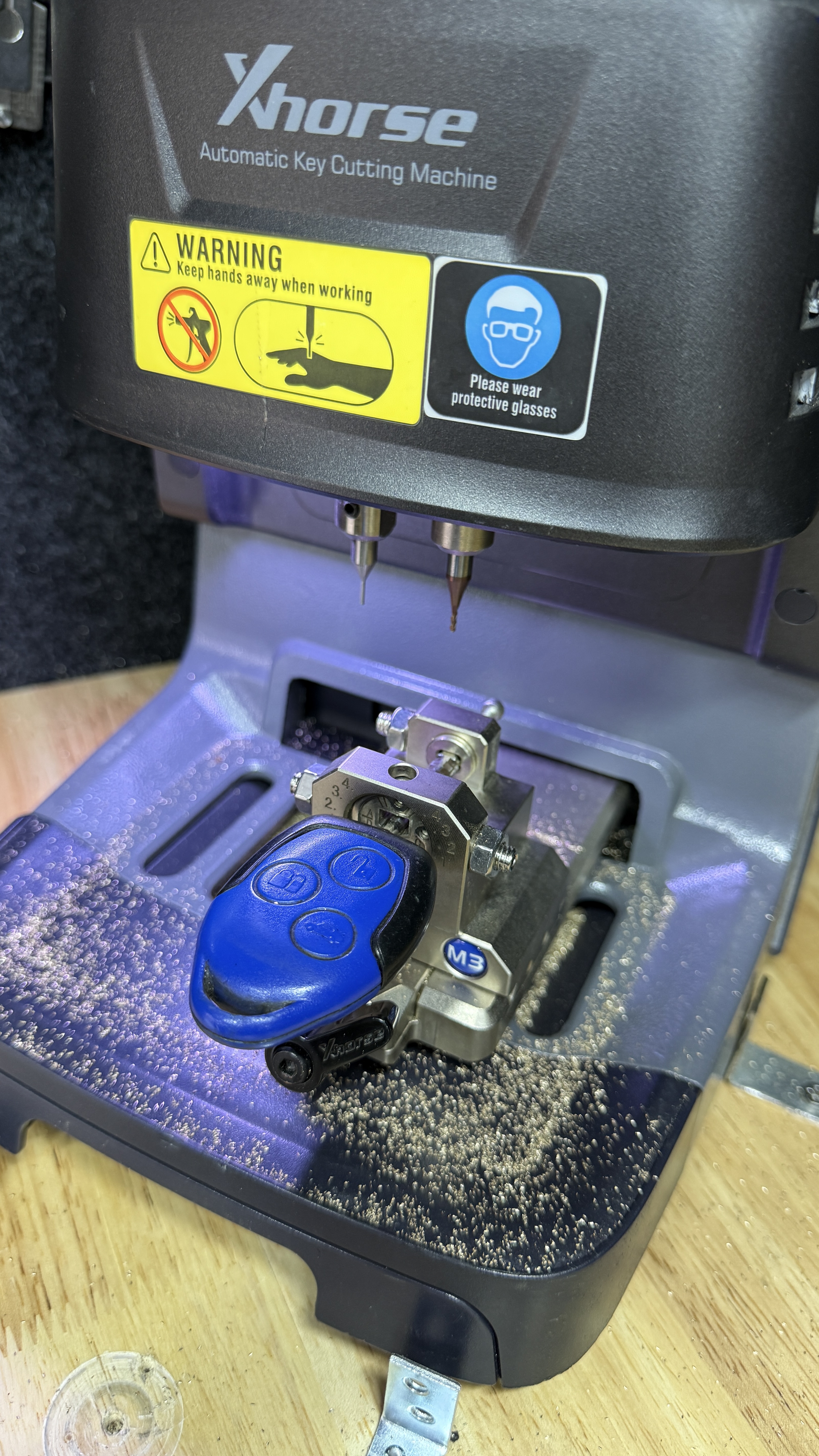 Xhorse automatic key-cutting machine with a car key fob secured in the clamp, used by KeyLogik