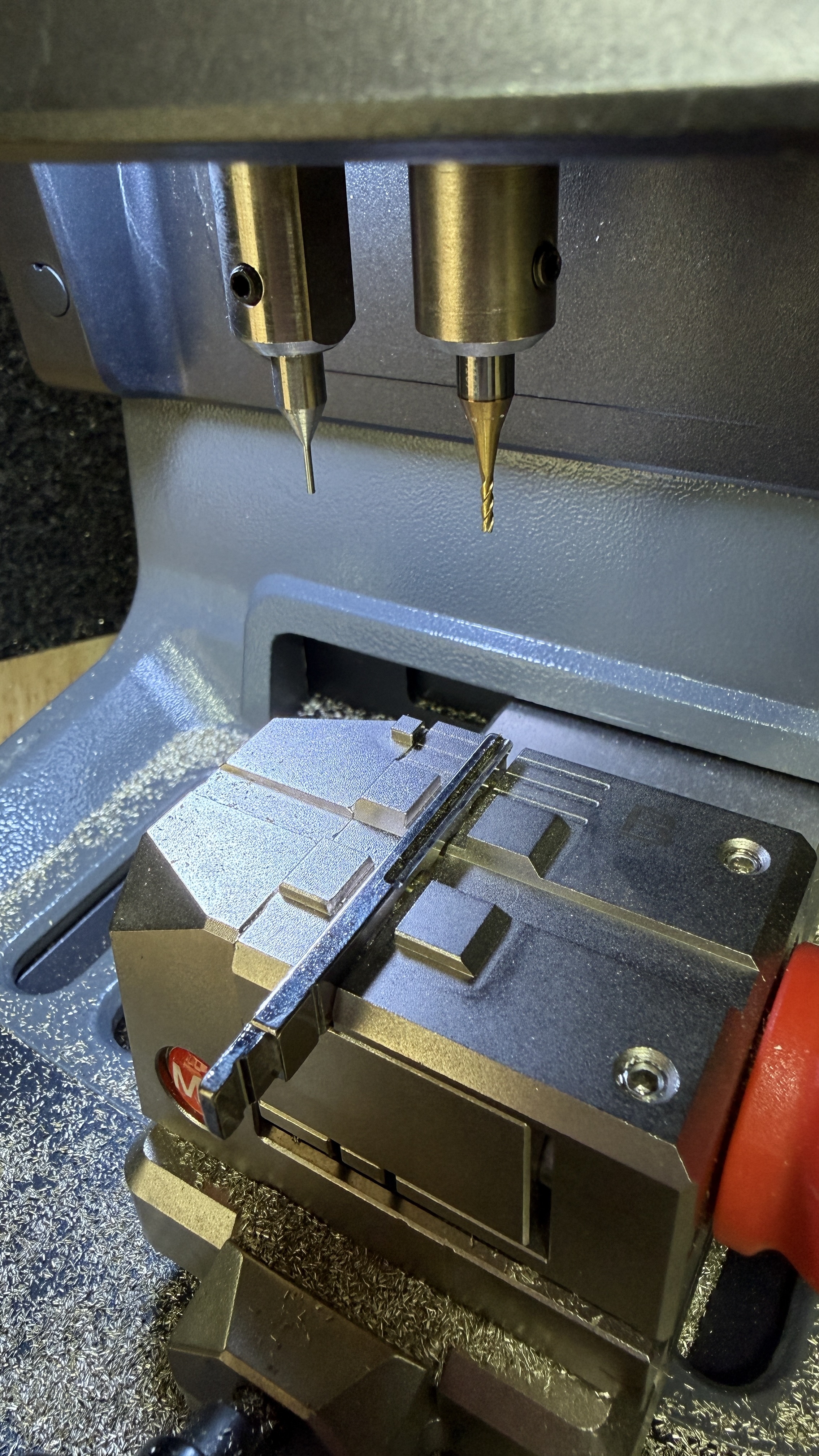 Car key blade in the cutting clamp under cool workshop lighting, KeyLogik mobile auto locksmith