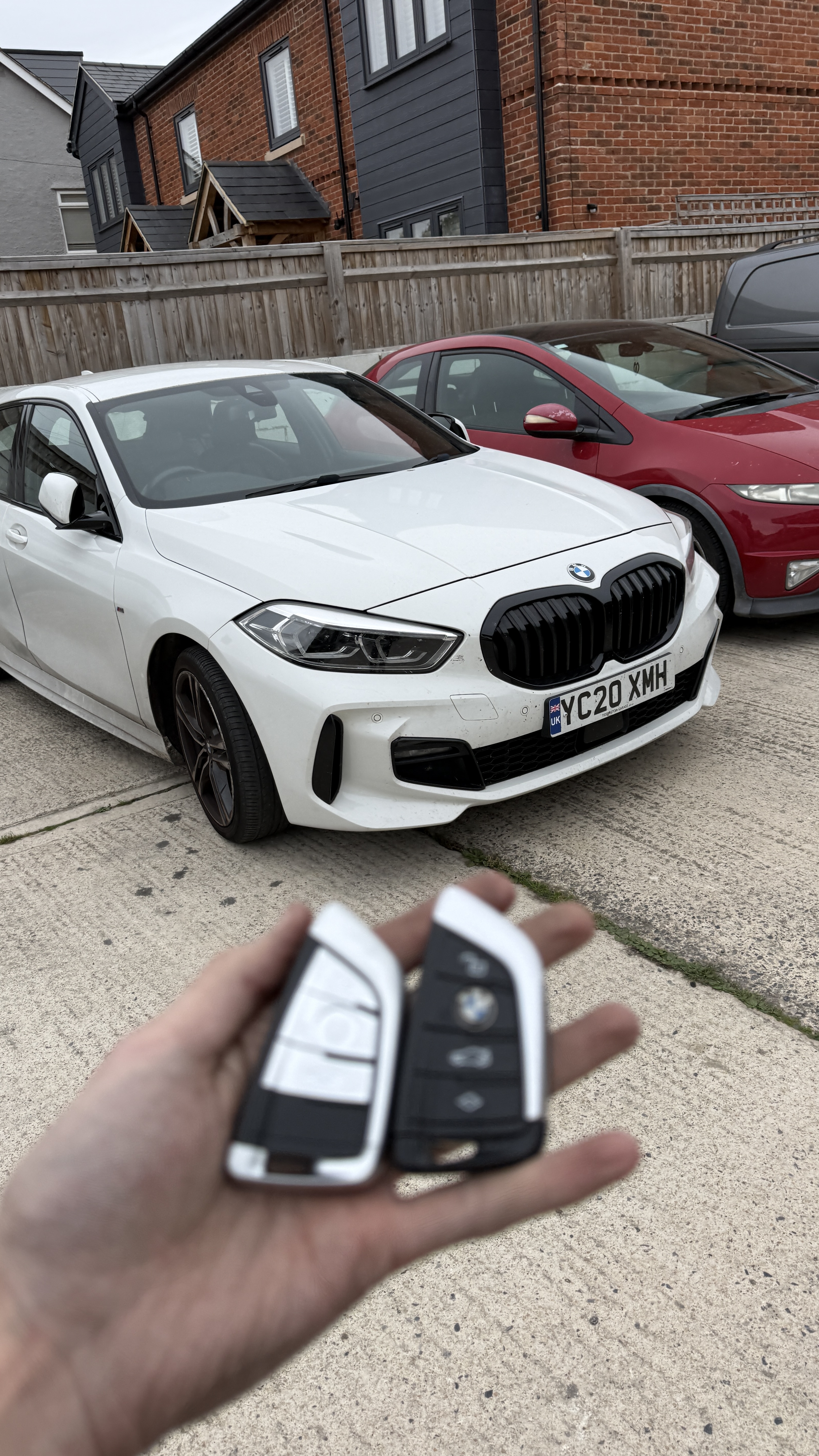 2020 BMW 1 Series spare key completed in Tiddington near Aylesbury Two BMW remote keys held in front of a white 2020 BMW 1 Series after a spare-key job in Tiddington near Aylesbury