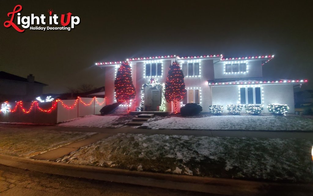 Full home Christmas light display with red and white roofline, lit trees and garland