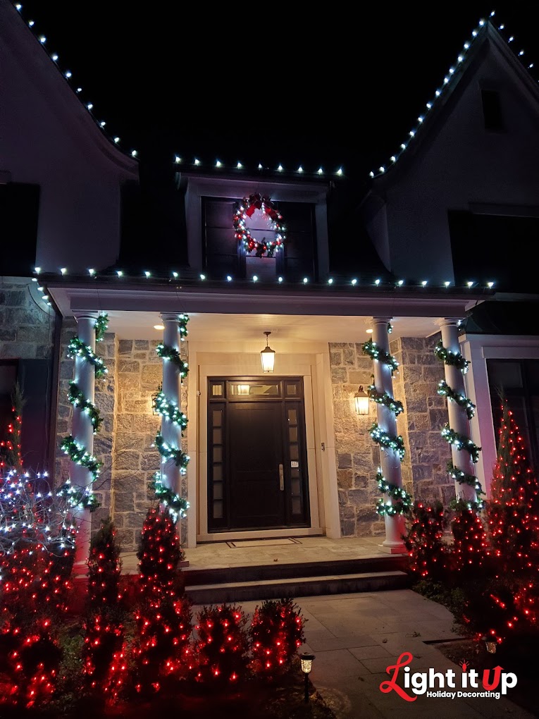 Stone home entrance with white roofline, garland columns, red bushes and wreath