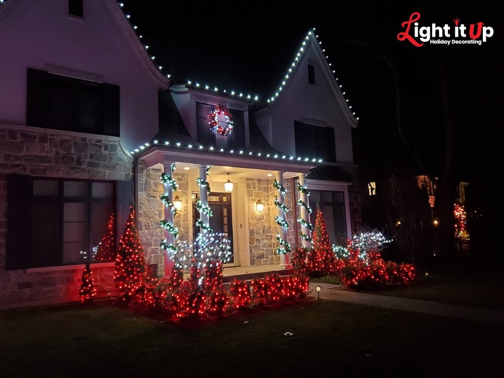 Stone home with white roofline lights, red bush lighting and garland columns
