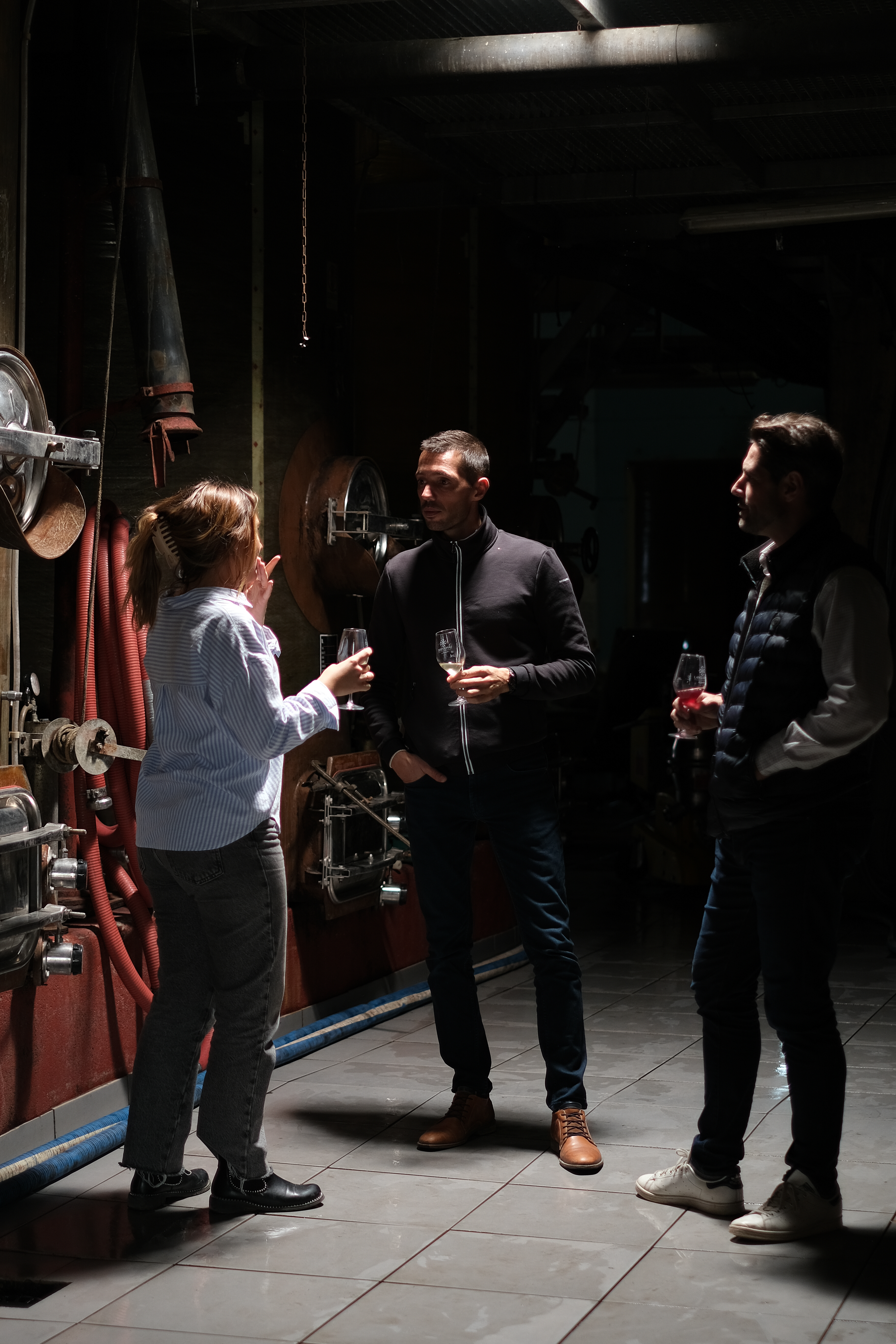 Camille échange avec deux visiteurs devant les foudres de la cave
