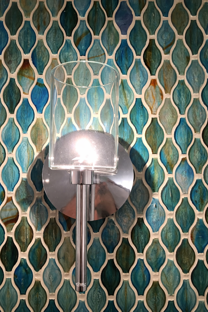 Wall sconce against a teal fish-scale mosaic tile wall