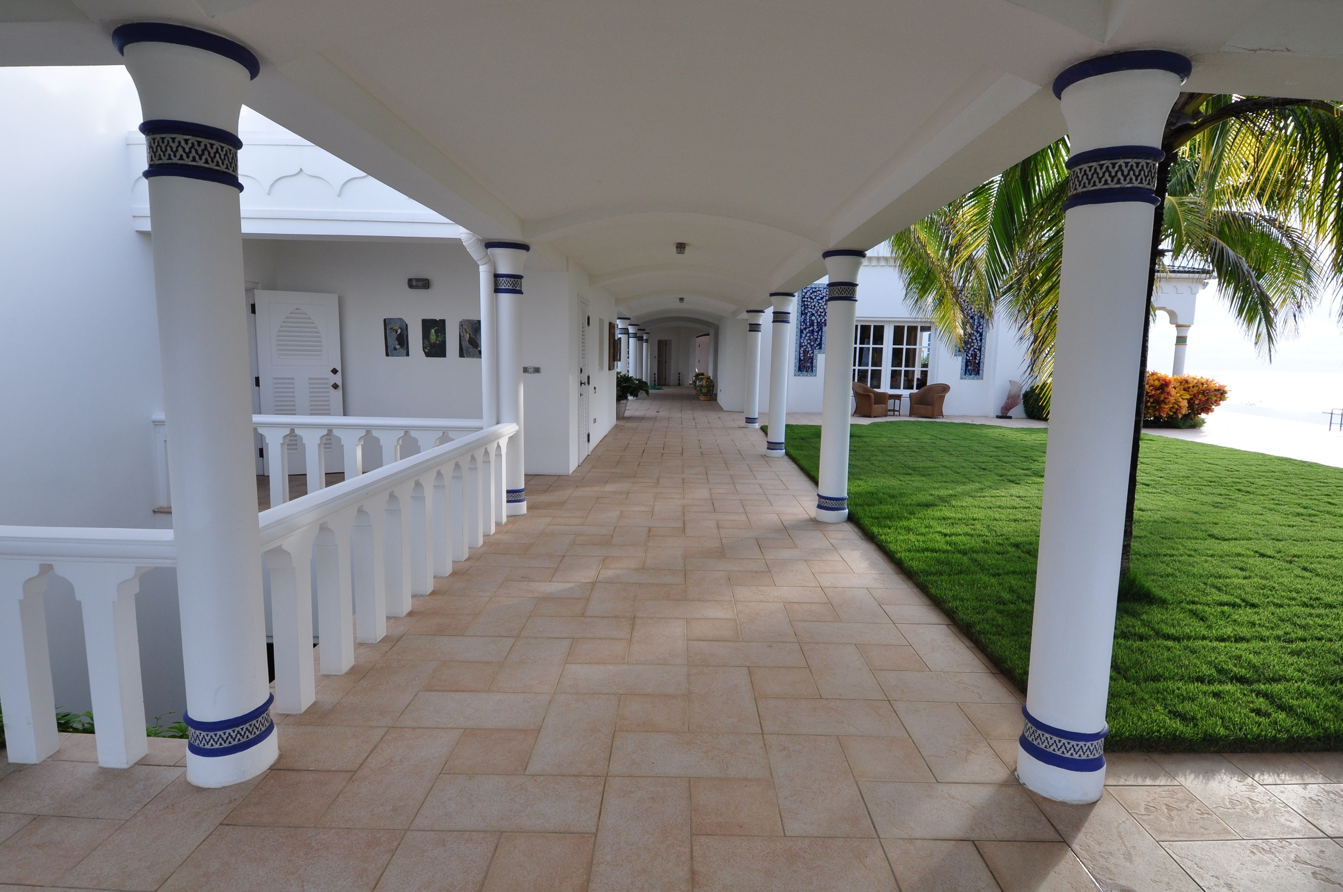 Covered colonnade with stone flooring, white columns and a view across the lawn to the ocean