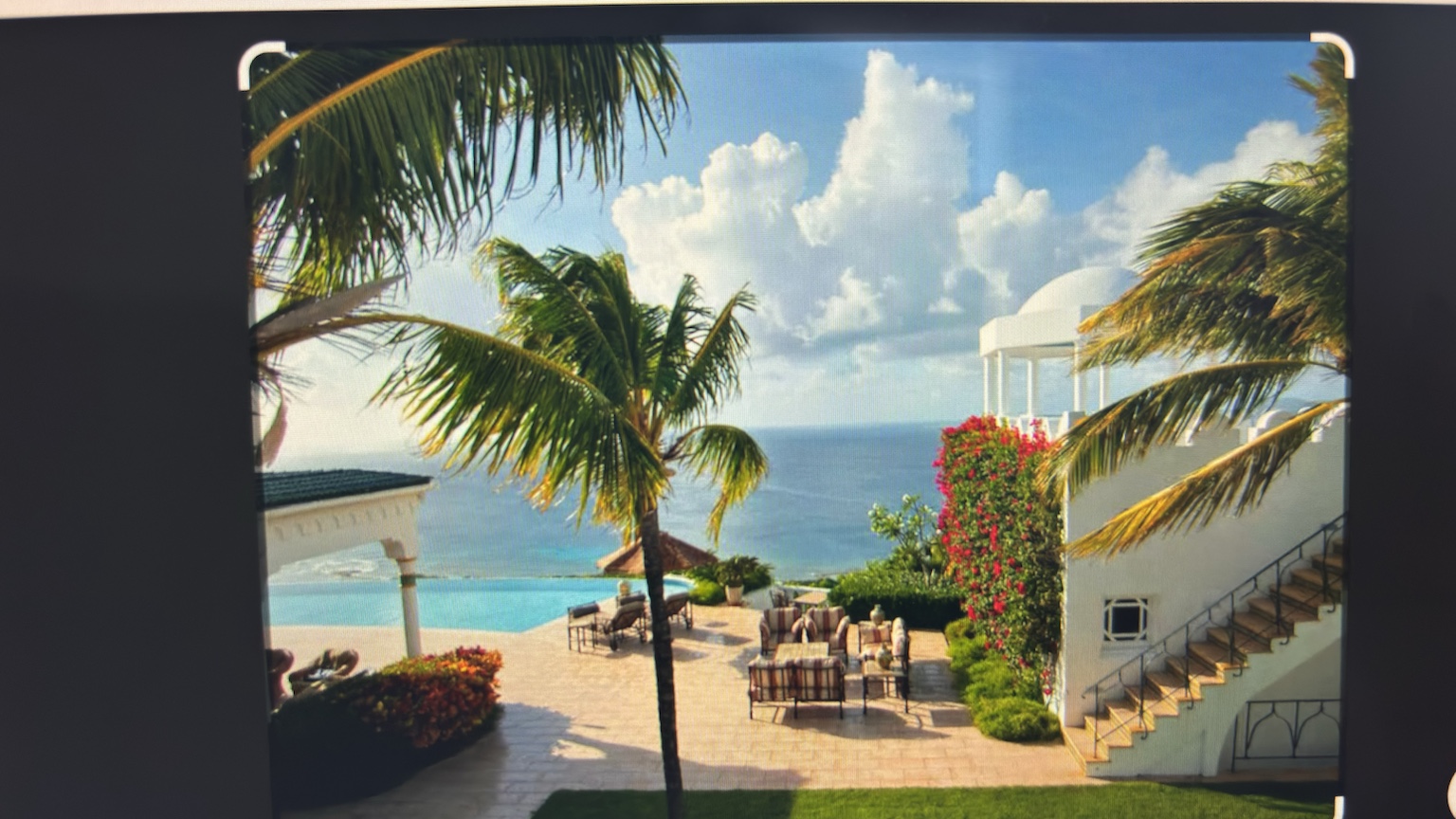 Oceanfront villa terrace with a pool, palm tree and bougainvillea-covered staircase above the sea
