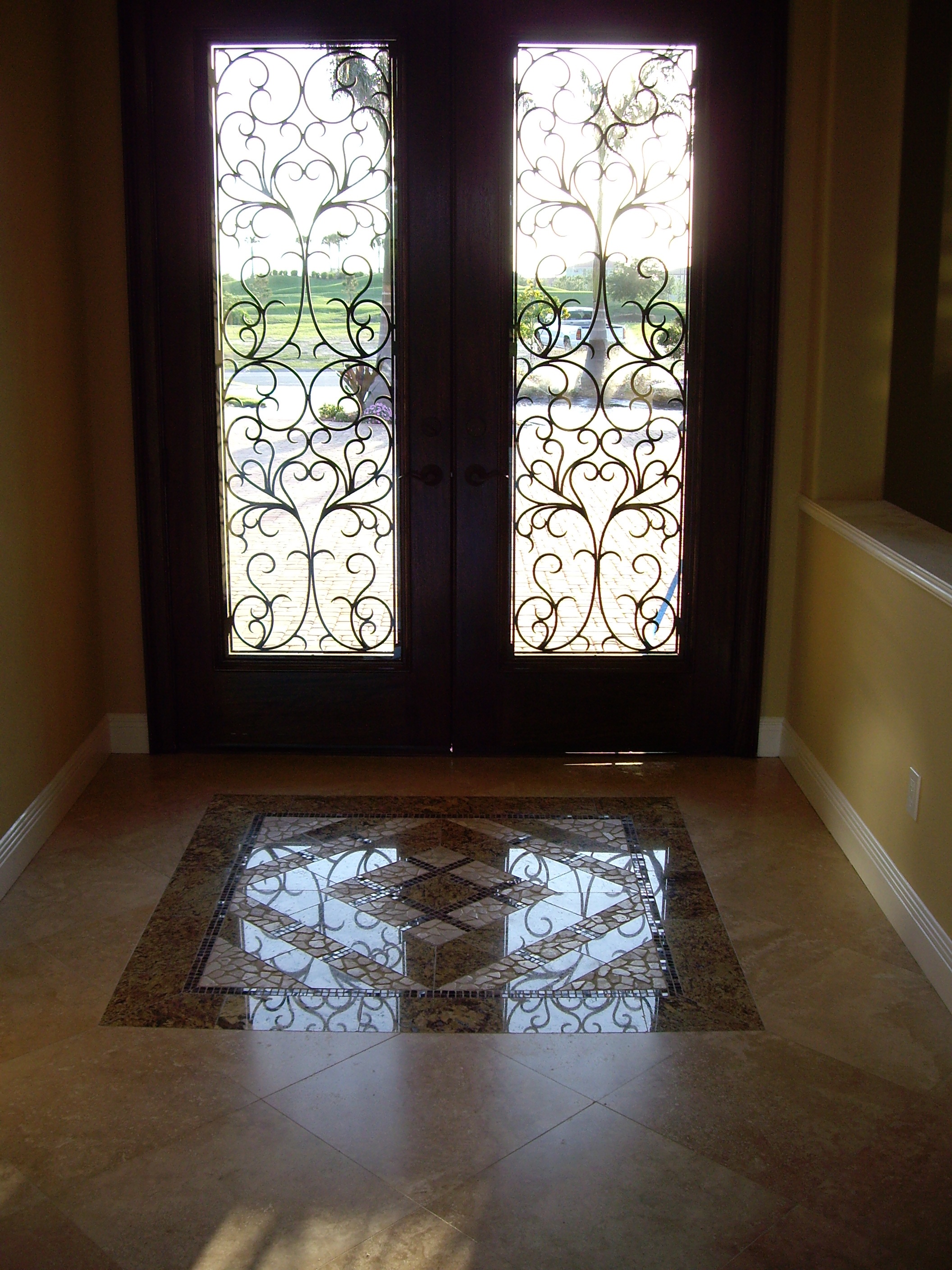 Foyer with a geometric stone mosaic medallion inlaid in a diamond-laid stone floor before arched double doors