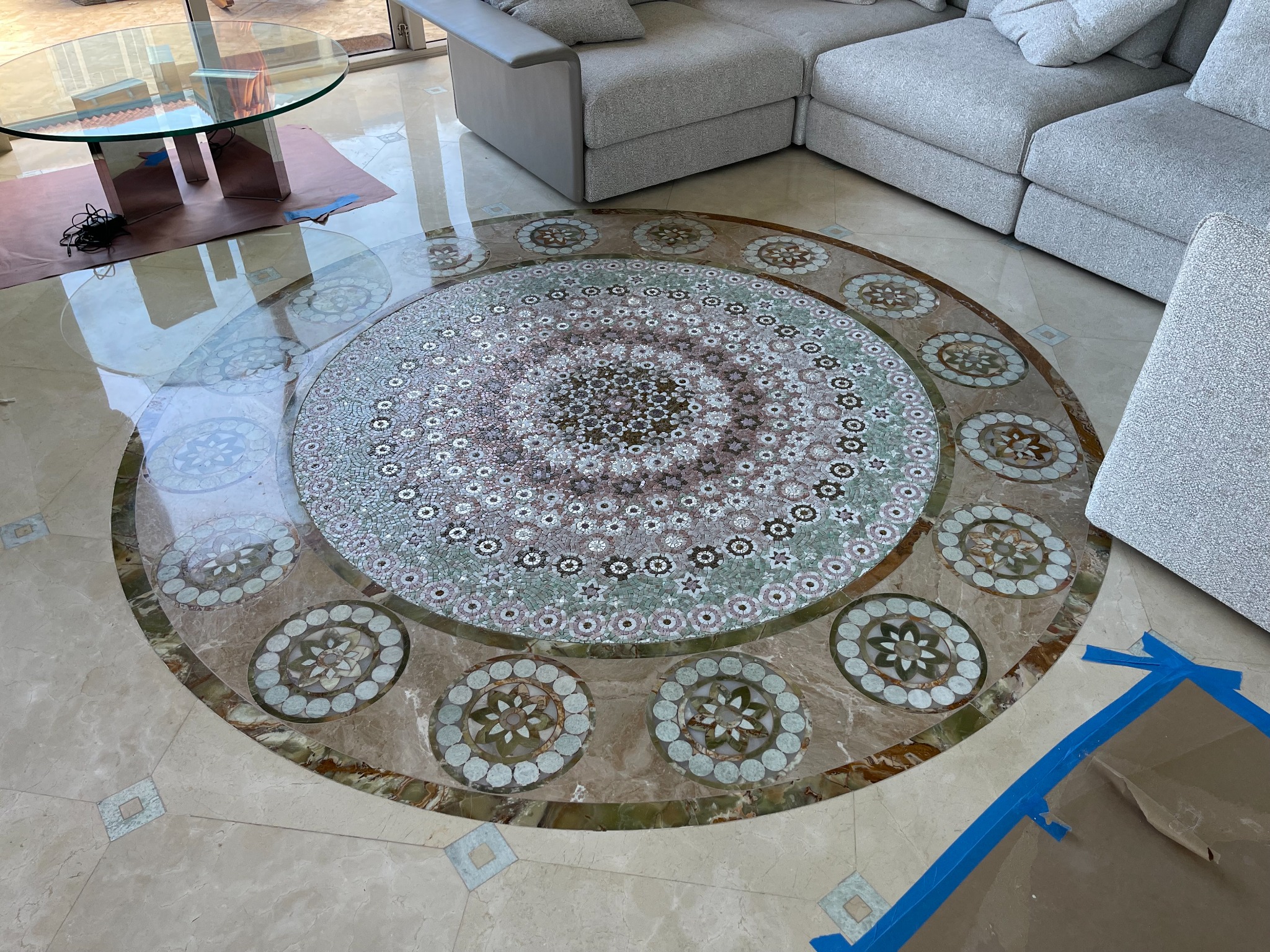 Circular stone and glass mosaic floor medallion inlaid in polished marble flooring