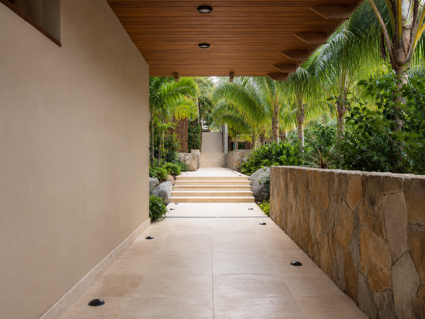 Covered outdoor walkway with large stone paving, a fieldstone wall and tropical planting