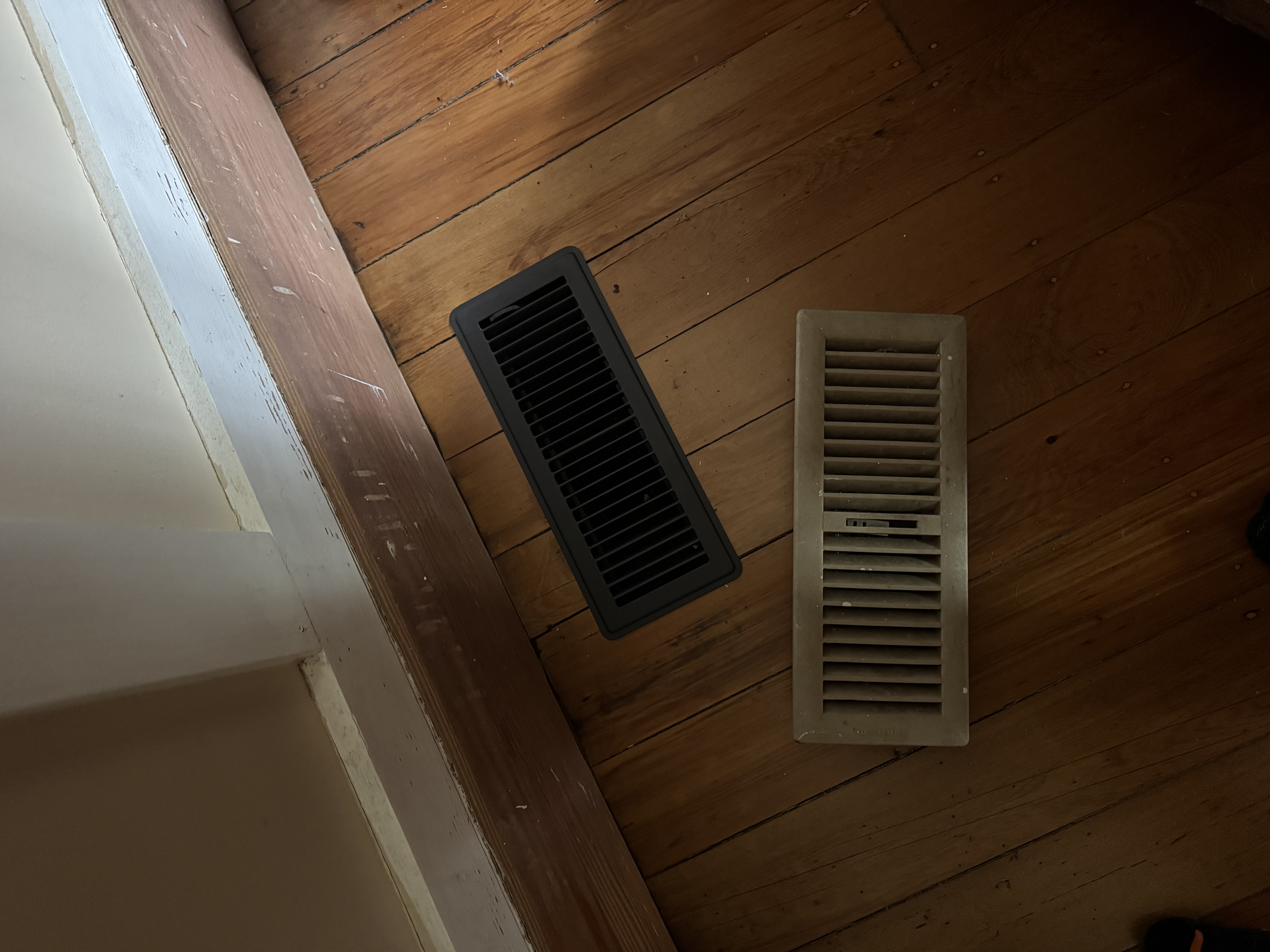 Black replacement floor register alongside an older register on a timber floor