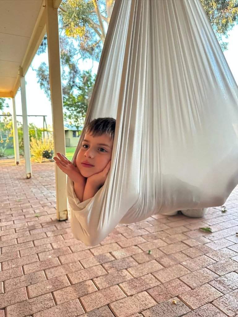 A boy resting inside a white fabric sensory swing outdoors