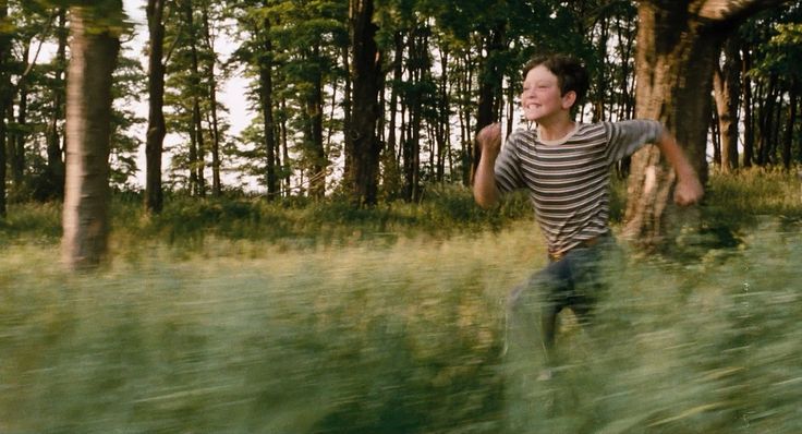 A boy running joyfully through a grassy field toward the trees