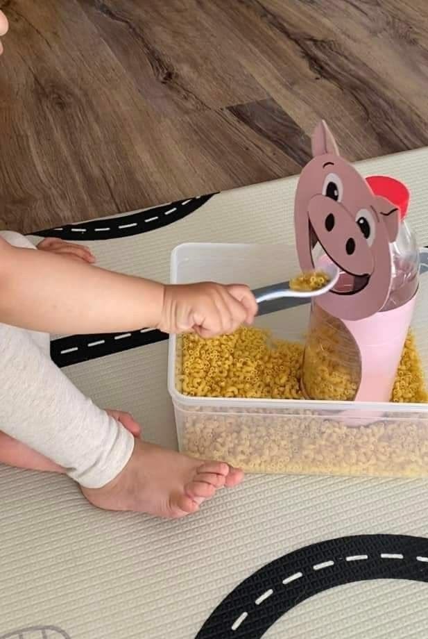 A child feeding dry macaroni into a cardboard pig
