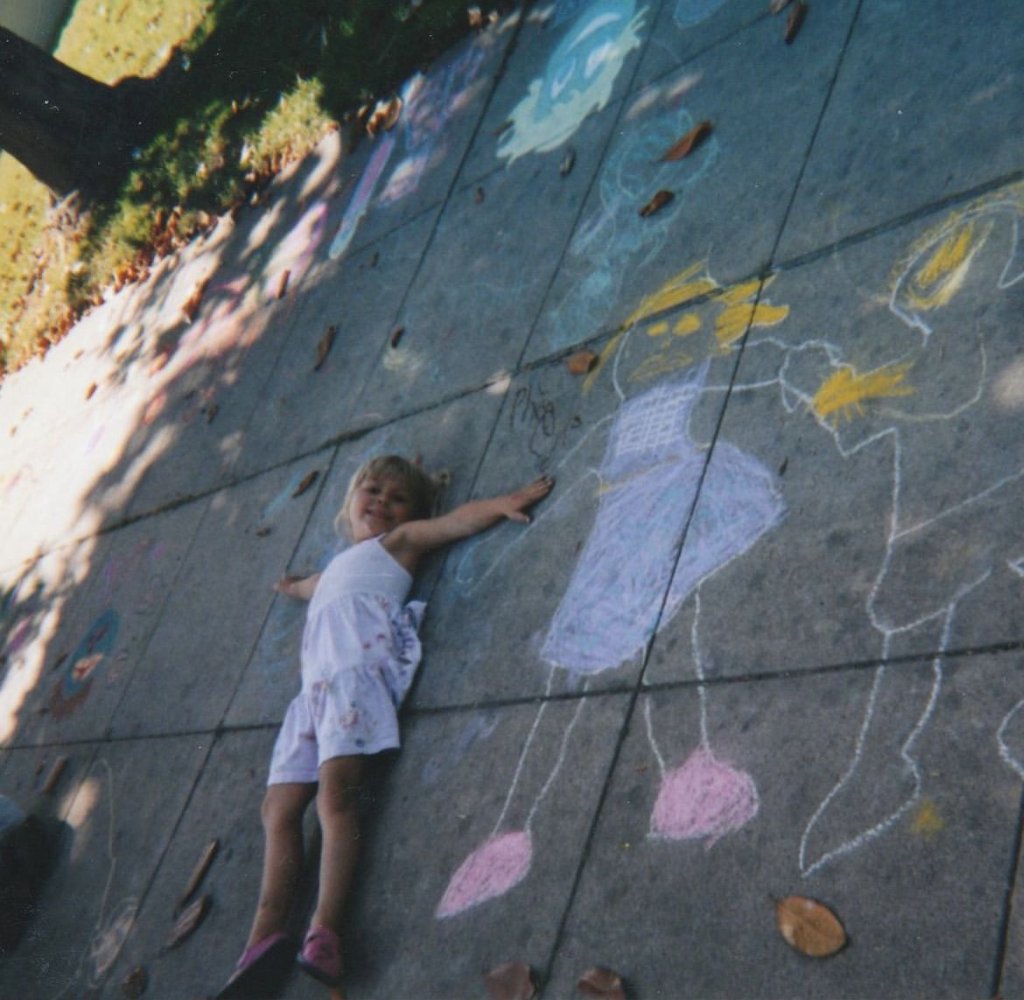 A girl lying on the pavement beside chalk figures she has drawn