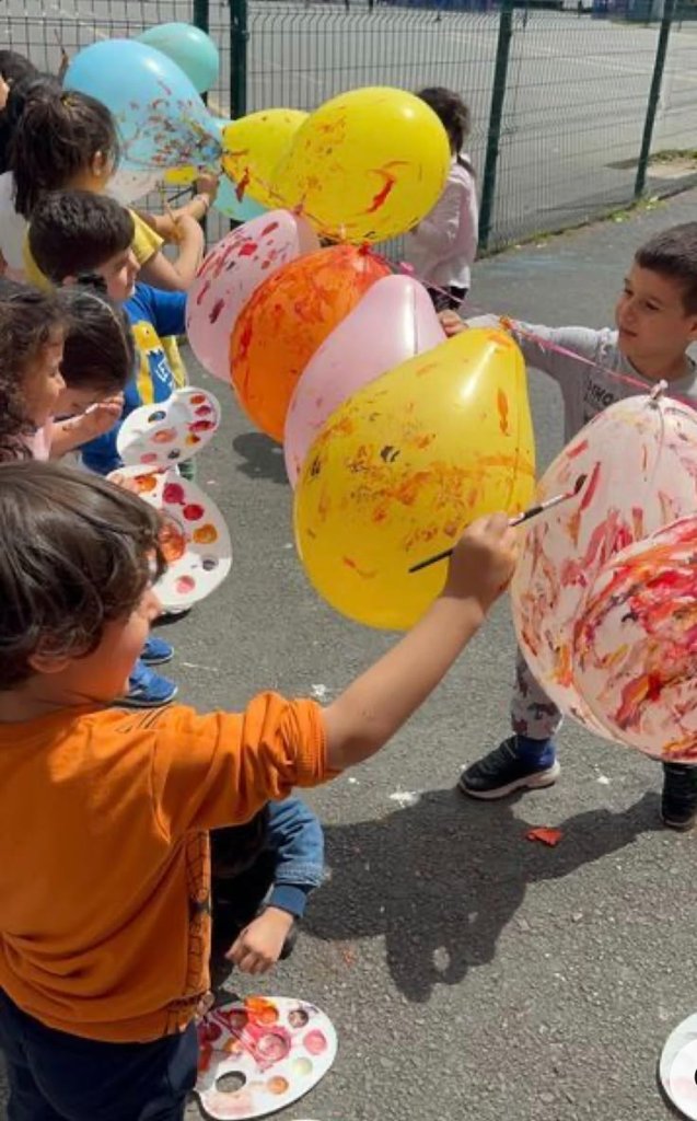 Children painting balloons outdoors with brushes and paint palettes
