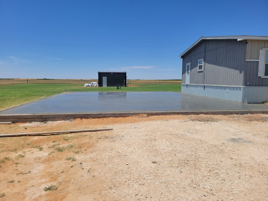 Freshly poured concrete garage slab with formwork beside a residential home