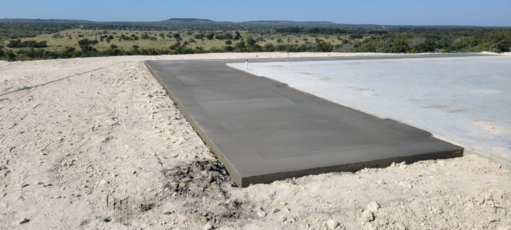 Freshly poured concrete slab with utility conduit on a rural job site