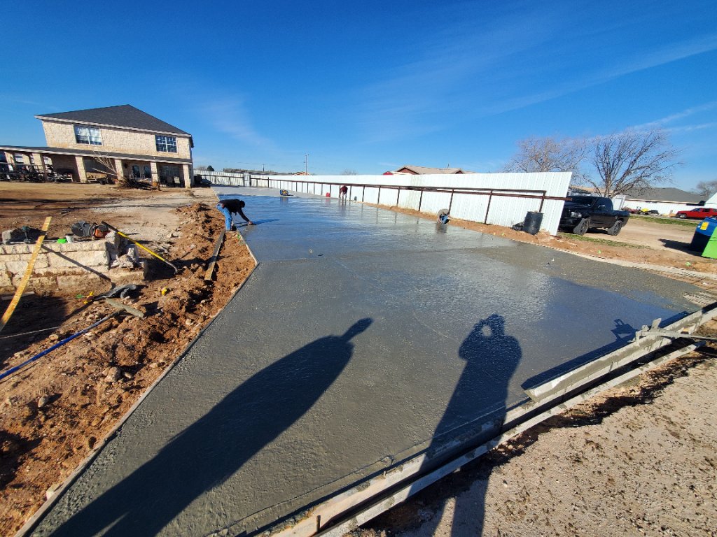 Freshly poured concrete driveway being finished on a sunny residential job site