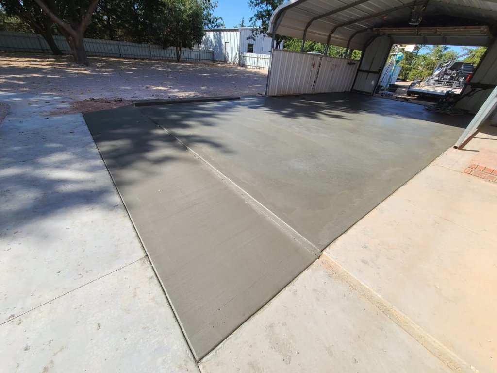 Concrete garage slab with an approach ramp beneath a metal carport structure