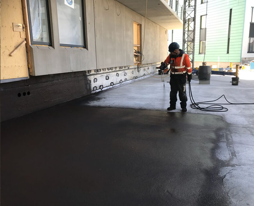 SprayGrade applicator spraying deck — two-component waterproofing system in progress