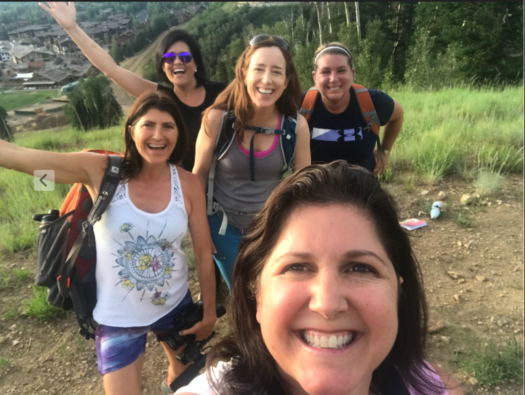 Group of five women hiking with backpacks, laughing on the trail