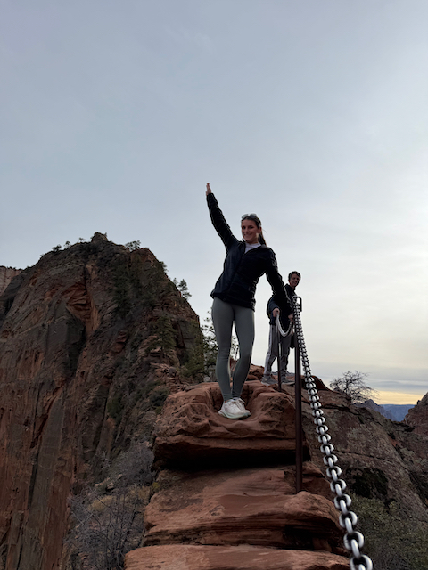 Hiker celebrating at the top of Angels Landing chain section at sunset
