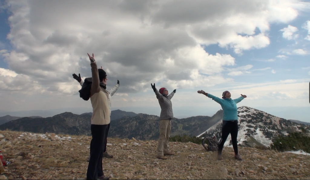 Three women with arms wide open on a mountain summit under dramatic cloudy sky